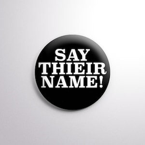 May include: A circular, black badge featuring the white text "SAY THEIR NAME!". The text is in a bold, sans-serif font. The badge has a glossy finish and a simple design.