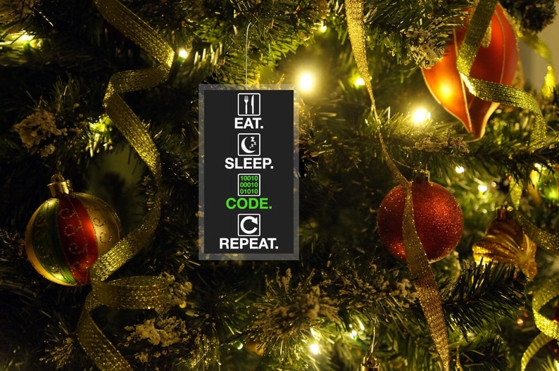 Pode incluir: Uma &aacute;rvore de Natal decorada com enfeites e fitas douradas. Um enfeite retangular com o texto "EAT. SLEEP. CODE. REPEAT." pendurado na &aacute;rvore. A palavra "CODE" est&aacute; escrita em c&oacute;digo bin&aacute;rio.