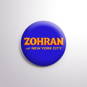 May include: A round, blue button with the name "ZOHRAN" in orange letters. Below the name, the text "FOR NEW YORK CITY" is written in white. The button is set against a white background.