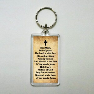 May include: A clear plastic keyring with a vintage-style paper insert featuring the Hail Mary prayer in black text on a tan background.