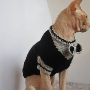 Pu&ograve; includere: Un gatto senza pelo che indossa un maglione di lana nero e grigio con un papillon. Il maglione ha un colletto e polsini grigi.