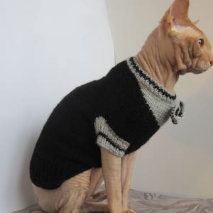 Pu&ograve; includere: Un gatto senza pelo che indossa un maglione di lana nero e grigio con un papillon.