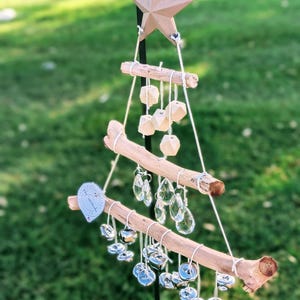 Peut inclure: Un carillon de Noël en bois en forme d'arbre avec une étoile au sommet. Le carillon a plusieurs niveaux avec des cristaux et des cloches métalliques qui pendent.