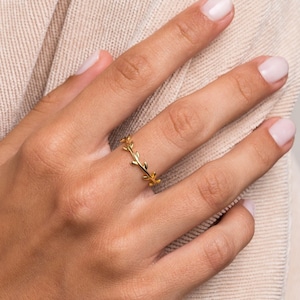 Può includere: Un anello d'oro con un delicato design a foglie. L'anello è indossato sul dito di una persona.