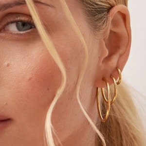 May include: A close-up of a person's ear with multiple gold hoop earrings. The earrings are stacked on top of each other, with the largest hoop at the bottom and the smallest hoop at the top.