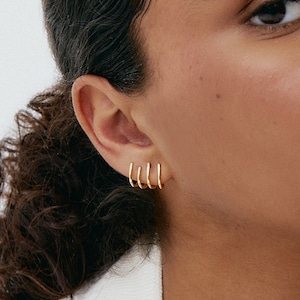 Peut inclure: Gros plan sur l'oreille d'une personne avec quatre boucles d'oreilles en or. Les boucles d'oreilles sont empilées les unes sur les autres, la plus petite en bas et la plus grande en haut.