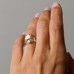 Könnte beinhalten: Ein goldener Ring mit einem Sonnenstrahlen-Design und einem kleinen Diamanten in der Mitte.