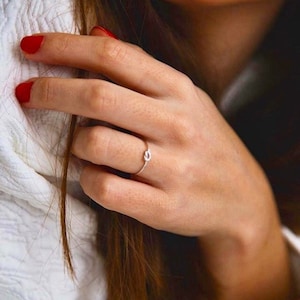 Può includere: Un anello d'argento con un design a nodo. L'anello è su un dito.