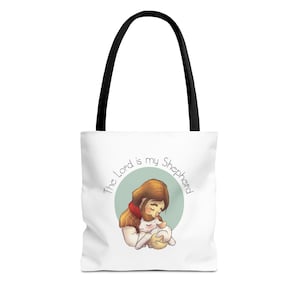 May include: White tote bag with black handles featuring an illustration of a person holding a lamb. The illustration is inside a light green circle, with the text "The Lord is my Shepherd" in a circular pattern around it.