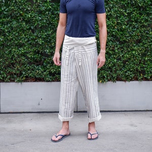 May include: A person wearing a navy blue short-sleeved t-shirt and striped, cropped pants. The pants are off-white with vertical black and blue stripes. The person is also wearing dark blue flip-flops.