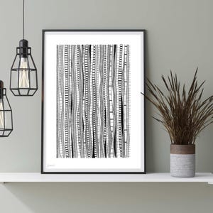 May include: Black and white abstract art print with a geometric pattern of lines and waves. The print is framed in a black frame and is hanging on a wall above a shelf.