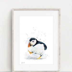 May include: Watercolor painting of a puffin standing on a white background with blue and gray watercolor splatters. The puffin is white with a black head and orange beak.