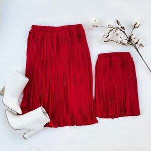 Może przedstawiać: Dwie czerwone plisowane sp&oacute;dnice, jedna długa, a druga kr&oacute;tka, wykonane z miękkiej, płynnej tkaniny. Sp&oacute;dnice są idealne na r&oacute;żne okazje, od codziennych po formalne.