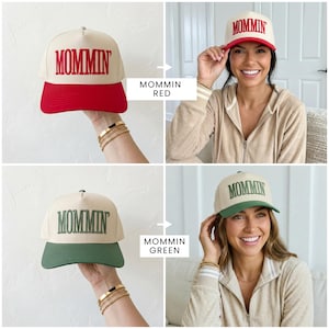 May include: Tan baseball cap with the word "MOMMIN" embroidered in red. The brim is red. Another cap has the word "MOMMIN" embroidered in green, with a green brim. The caps are shown in a lifestyle setting.