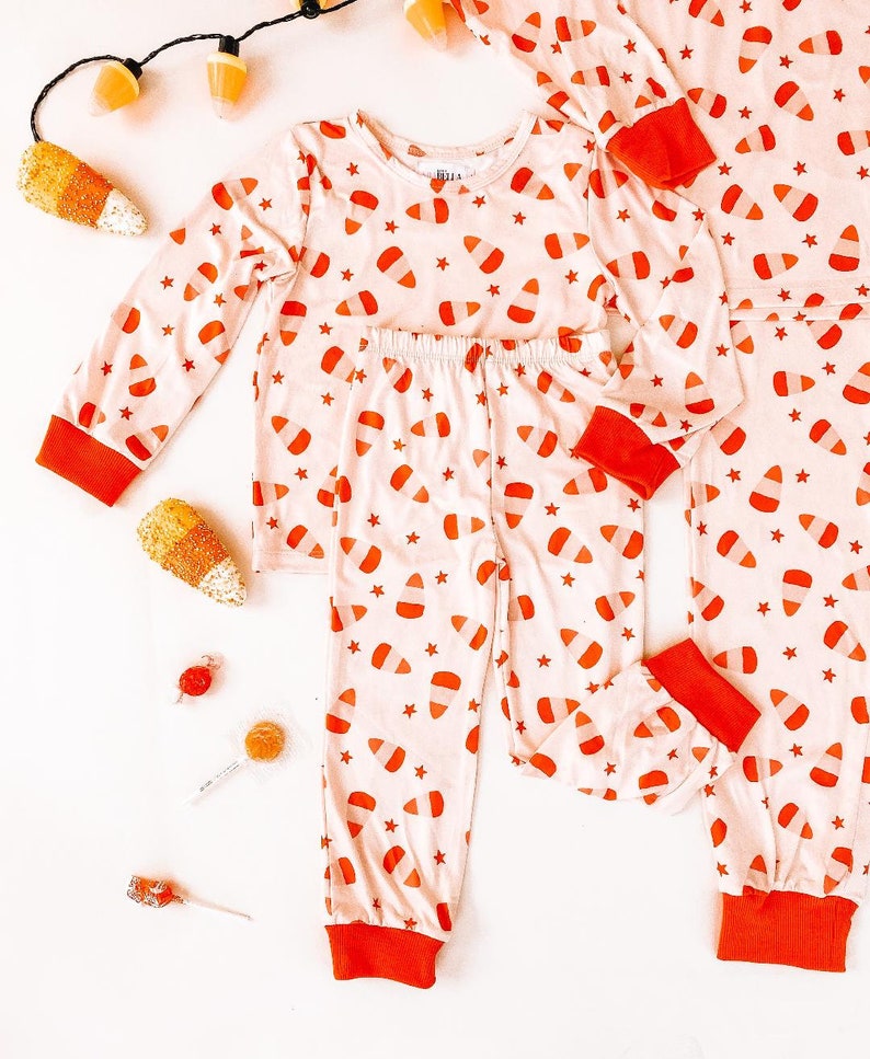 May include: A set of pajamas with a candy corn print. The pajamas are pink with orange and white candy corn designs and red trim.