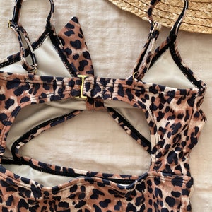 Pu&ograve; includere: Un costume da bagno intero con stampa leopardata. Il costume presenta spalline regolabili, una chiusura color oro e un design con schiena scoperta. I colori sono marrone, nero e beige.