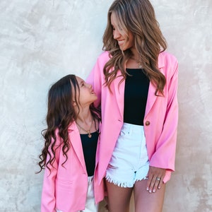 May include: Two people wearing pink blazers and white shorts. The person on the left is a child and the person on the right is an adult. Both are looking at each other and smiling.