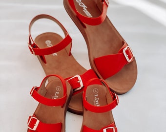 May include: Three pairs of red sandals with gold buckles. The sandals have a brown sole and are made of a soft, comfortable material. The sandals are available in sizes 4 and 7.