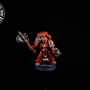 Può includere: Una miniatura dipinta di rosso e argento di un marine spaziale che brandisce un'ascia a catena. La miniatura è in piedi su una base nera.