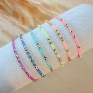 May include: Seven colorful beaded bracelets with silver beads. The bracelets are arranged in a rainbow order, from purple to pink, blue, green, yellow, orange, and red.