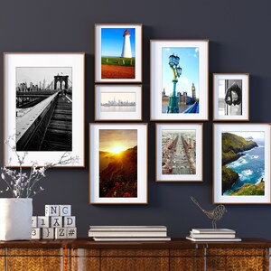 K&ouml;nnte beinhalten: Eine Wandgalerie mit neun gerahmten Fotografien verschiedener Stadt- und Landschaftsbilder. Die Fotos zeigen ein Schwarzwei&szlig;bild der Brooklyn Bridge, einen Leuchtturm an einer felsigen K&uuml;ste, eine Skyline mit Wolkenkratzern, eine Stra&szlig;enszene mit Autos, eine Ansicht einer Stadt mit einer Br&uuml;cke und einer Stra&szlig;enlaterne sowie eine K&uuml;stenlandschaft mit einer felsigen K&uuml;ste und blauem Wasser.