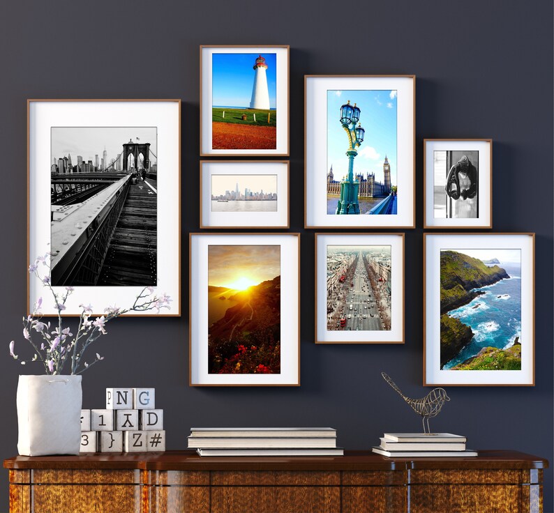 K&ouml;nnte beinhalten: Eine Wandgalerie mit neun gerahmten Fotografien verschiedener Stadt- und Landschaftsbilder. Die Fotos zeigen ein Schwarzwei&szlig;bild der Brooklyn Bridge, einen Leuchtturm an einer felsigen K&uuml;ste, eine Skyline mit Wolkenkratzern, eine Stra&szlig;enszene mit Autos, eine Ansicht einer Stadt mit einer Br&uuml;cke und einer Stra&szlig;enlaterne sowie eine K&uuml;stenlandschaft mit einer felsigen K&uuml;ste und blauem Wasser.