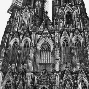 K&ouml;nnte beinhalten: Ein Schwarzwei&szlig;foto des K&ouml;lner Doms in Deutschland. Der Dom ist ein gro&szlig;es gotisches Bauwerk mit zwei hohen T&uuml;rmen. Die Vorderseite des Doms ist mit aufwendigen Schnitzereien und Buntglasfenstern verziert. Vor dem Dom gehen Menschen spazieren.