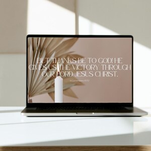 May include: A laptop screen displaying a beige background with a quote from the Bible: "But thanks be to God! He gives us the victory through our Lord Jesus Christ." The quote is from 1 Corinthians 15:57. A candle is in the background.