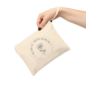 Może przedstawiać: Beżowa kosmetyczka z zamkiem błyskawicznym z czarno-białym logo z napisem "Seeds of Truth Designs" i przedstawiającym kwiat oraz tekst "Sowing Seeds of the Gospel".