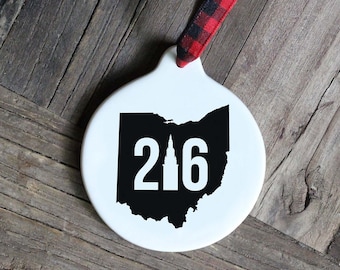 Puede incluir: Adorno de cerámica blanca con una silueta negra del estado de Ohio y el número 216 en su interior. El adorno tiene una cinta a cuadros rojos y negros.