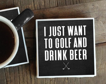Puede incluir: Dos posavasos negros con texto blanco. El posavasos superior dice "Solo quiero jugar al golf y beber cerveza" con un par de palos de golf cruzados debajo del texto. El posavasos inferior tiene una taza de café encima.