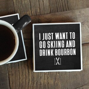 May include: Two black and white coasters with a white background and black text. The top coaster says "I just want to go skiing and drink bourbon" with a stylized "IXI" below the text. The bottom coaster has a cup of coffee on it.