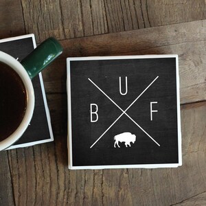 May include: Two black and white coasters with a white buffalo silhouette and the letters "BUF" in a cross pattern. One coaster has a cup of coffee on top of it.