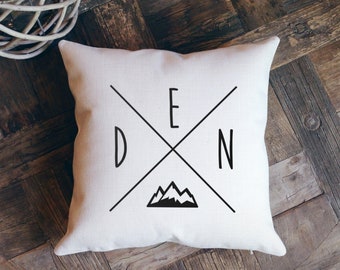 Puede incluir: Almohada blanca con texto negro que dice "DEN" con un gráfico de montaña y una X negra en el centro.