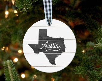 May include: White round ornament with a black and white checkered ribbon. The ornament features a black silhouette of the state of Texas with the word "Austin" written in white cursive.
