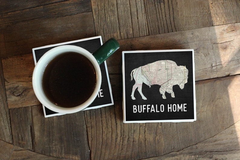 May include: Two black and white coasters with a white border. One coaster features a silhouette of a buffalo with a map pattern inside. The other coaster has the text "BUFFALO HOME".