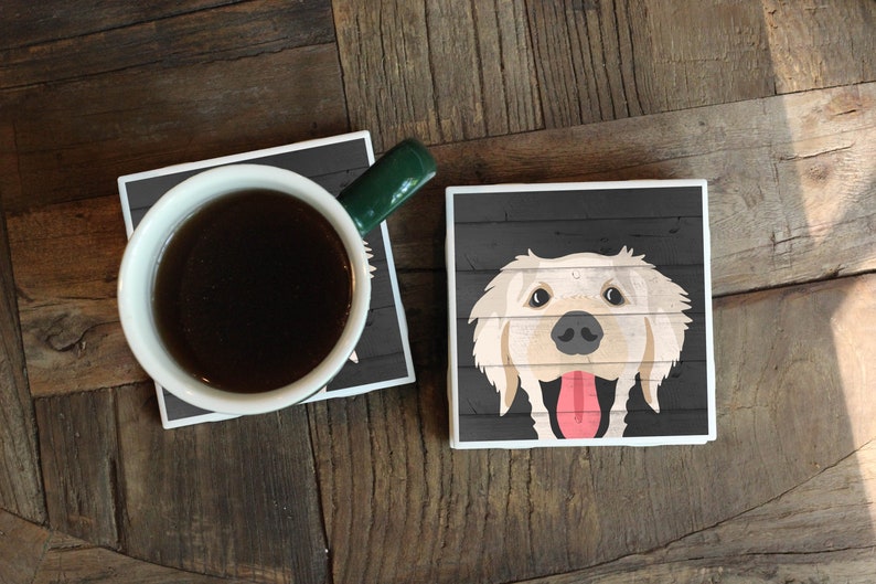 Puede incluir: Dos posavasos cuadrados de cer&aacute;mica con fondo de madera negra. Un posavasos presenta una imagen de dibujos animados de un perro golden retriever con la lengua fuera. El otro posavasos tiene una taza de caf&eacute; encima.