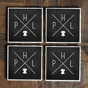 May include: Set of four black square coasters with white lettering and a Liberty Bell graphic. The coasters feature the letters "H", "P", "L" arranged in a cross pattern.