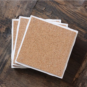 May include: A set of three cork coasters with a white border. The coasters are stacked on top of each other on a wooden surface.