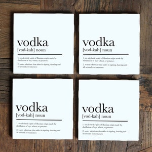 May include: Four white square coasters with black text that reads "vodka [vod-kah] noun" and a definition of the word. The coasters are arranged in a 2x2 grid on a wooden surface.