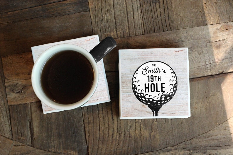 square waterproofing mug coasters made from ceramic tile and cork adhered to the bottom, print your chosen name and phrase "19th Hole" on a background has golf ball image