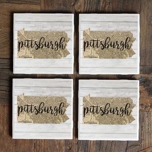 May include: Set of four white ceramic coasters featuring a vintage map of Pittsburgh, Pennsylvania, with the word "pittsburgh" in black script.