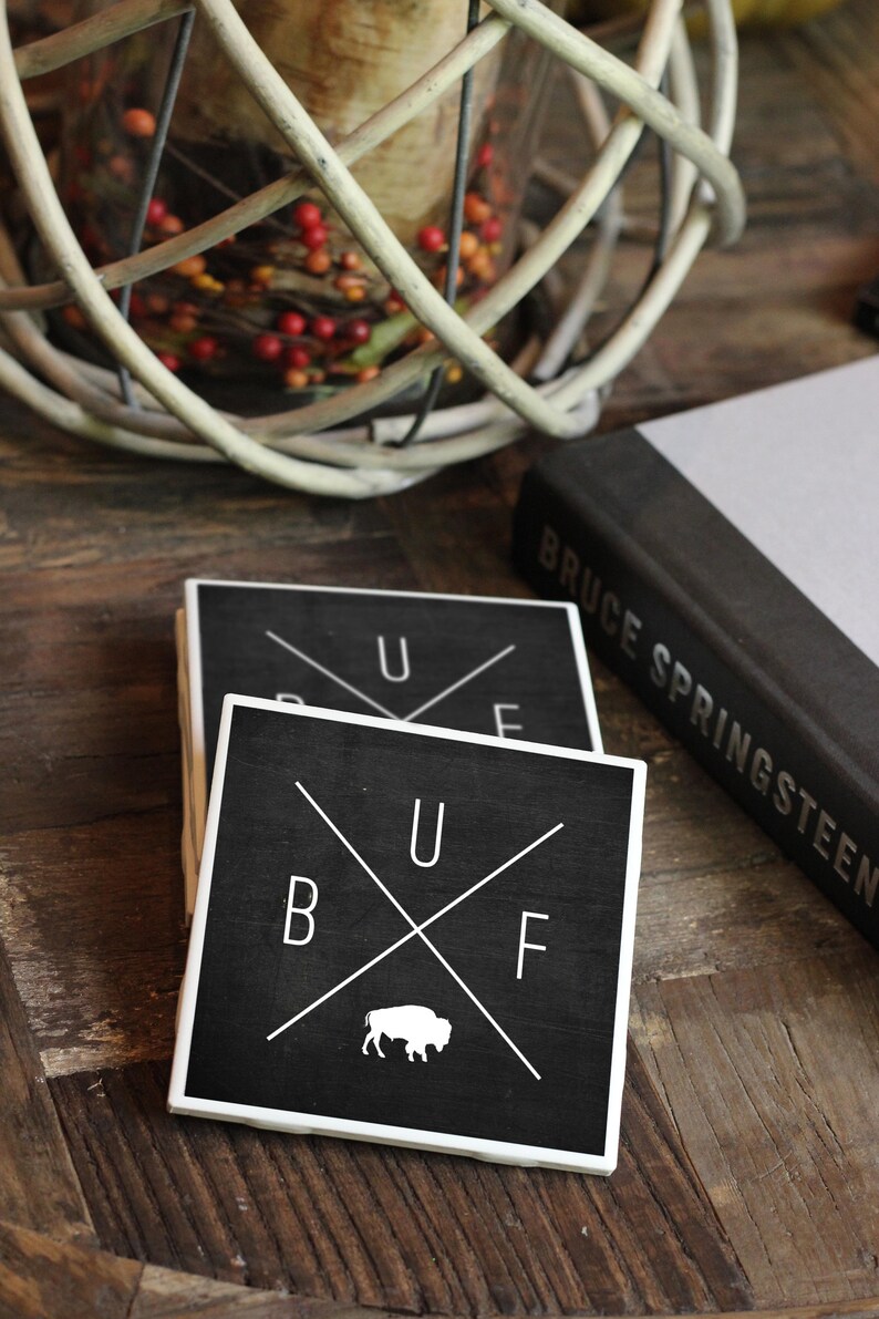 May include: Two black square coasters with white lettering and a white buffalo silhouette. The top coaster says "U F" and the bottom coaster says "B U F".
