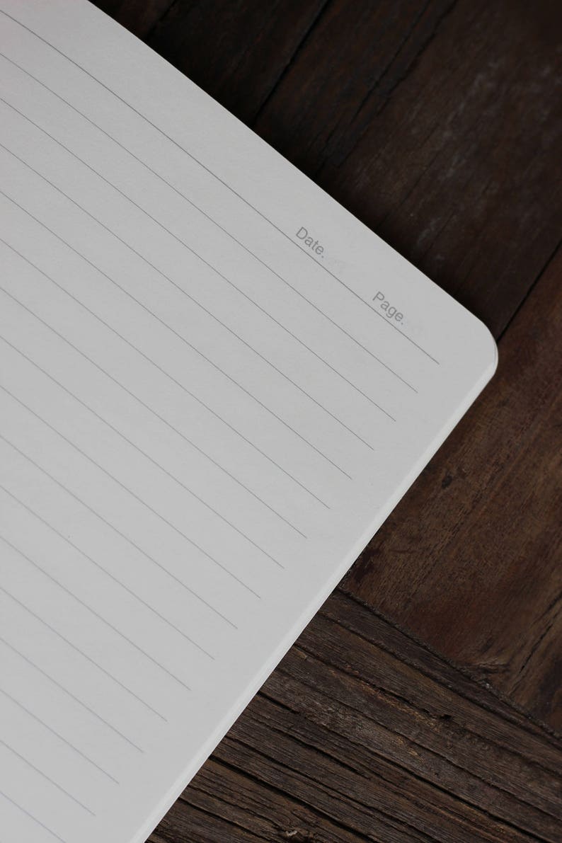 May include: A blank, lined notebook with the words "Date" and "Page" printed at the top of the page. The notebook is lying open on a dark brown wooden surface.