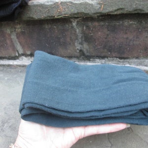 May include: A pair of dark blue tights folded in half, held in a hand.
