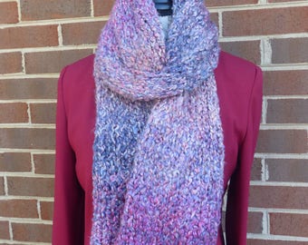 May include: A soft, knitted scarf in shades of purple, pink, and blue. The scarf is made of a chunky yarn and has a textured look.
