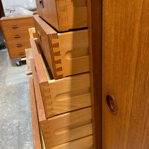 May include: A wooden dresser with five drawers and a sliding door. The drawers are open and show the dovetail joinery. The dresser is made of a light wood with a natural finish.