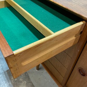 May include: A wooden dresser with a drawer open, revealing a green felt lining. The drawer has a wooden divider and a wooden handle. The dresser has a wood grain finish and a light brown color.