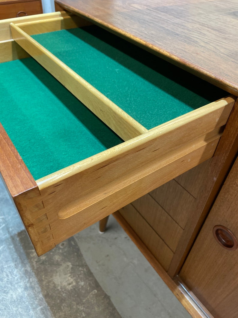 May include: A wooden dresser with a drawer open, revealing a green felt lining. The drawer has a wooden divider and a wooden handle. The dresser has a wood grain finish and a light brown color.