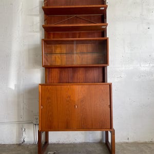 Op de afbeelding: Een teak houten kast in mid-century modern stijl met een glazen vitrine en twee deuren. De kast heeft een warme bruine kleur en een eenvoudig, elegant ontwerp.